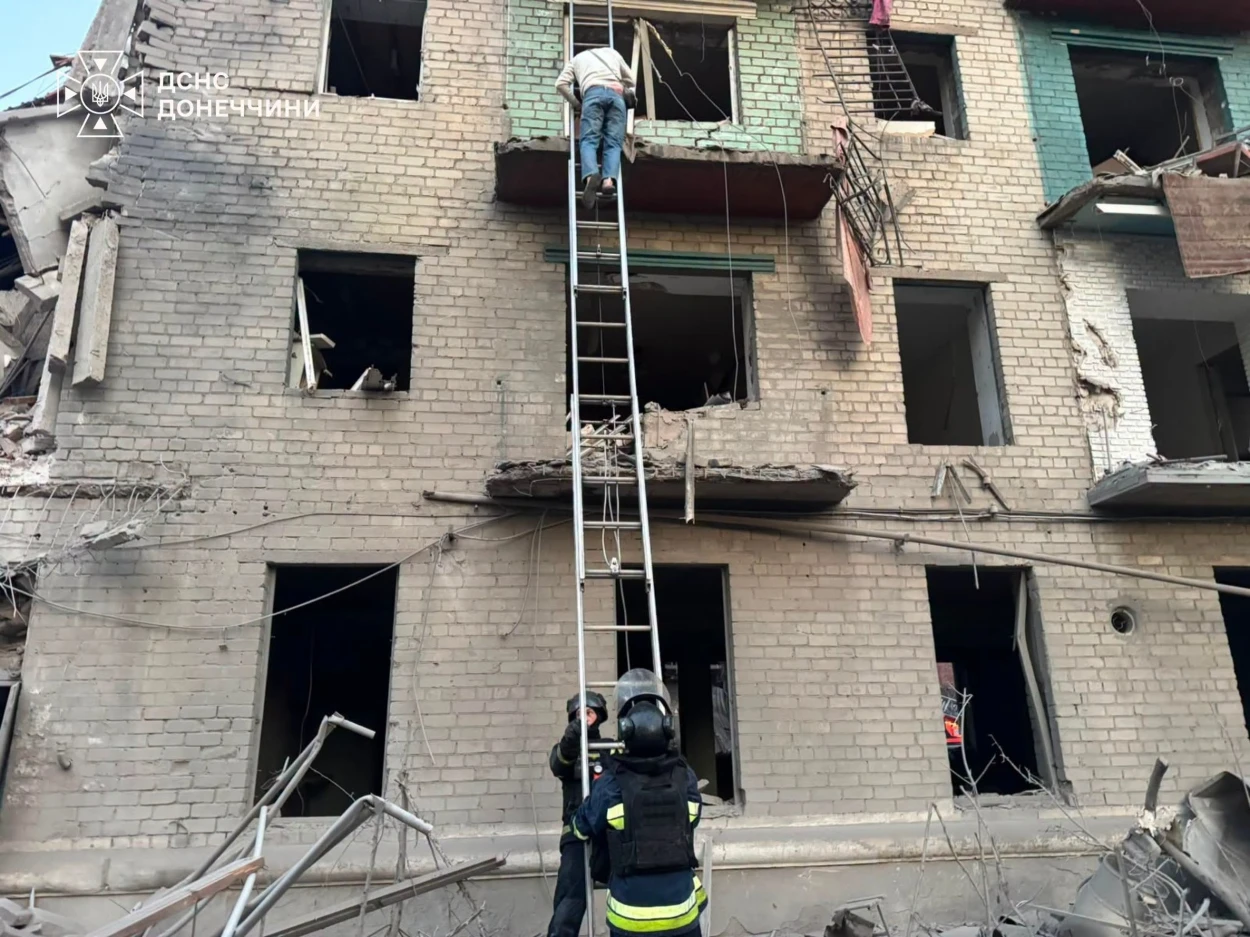 Слов’янськ після російського авіаудару 26 серпня. На фото рятувальники біля пошкодженої багатоповерхівки з вибитими вікнами та зруйнованими балконами, один із чоловіків спускається драбиною з квартири