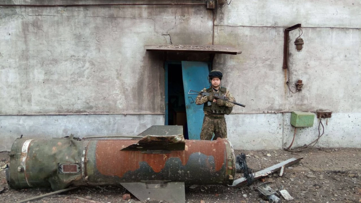 «Черрі» у військовій формі та зі зброєю стоїть біля пошкодженої будівлі в Маріуполі, на передньому плані лежать уламки ракети