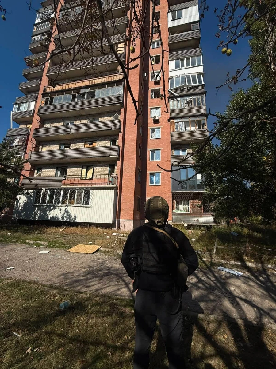 Пошкоджена обстрілом багатоповерхівка - розбиті вікна, навколо фанера і скло, уламки