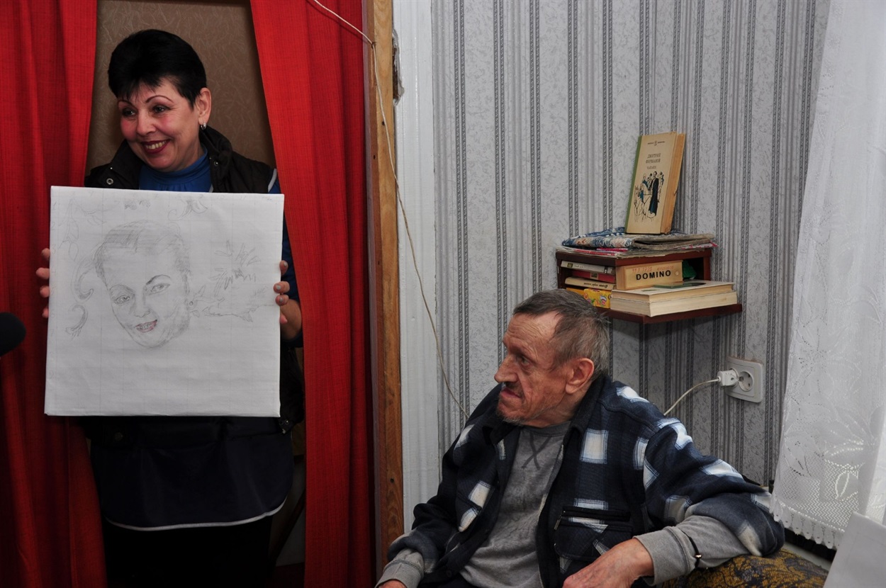 Ирина Шулимова показывает свой портрет, который нарисовал Анатолий 