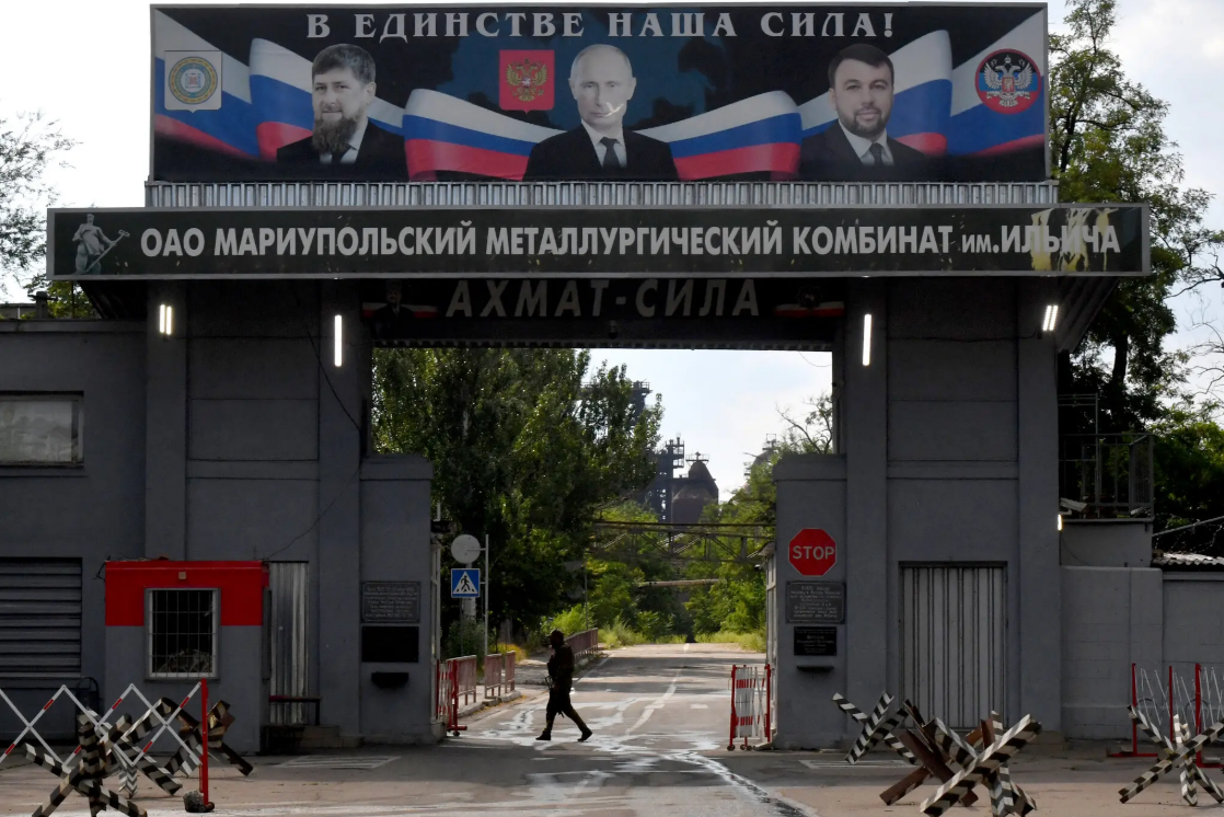 Вхід до металургійного комбінату імені Ілліча, ще одного заводу в Маріуполі, липень 2025. На банері зображені портрети Рамзана Кадирова, лідера Чечні, президента Росії Володимира Путіна та Дениса Пушиліна, глави Донецької області в Україні.