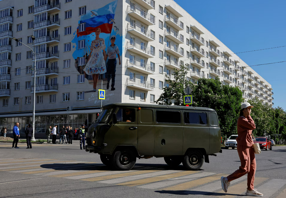 Мурал, прикрашений на будівлі, присвячений третій річниці взяття Росією контролю над Маріуполем, височіє над мешканцями окупованого українського міста у травні 2025 року