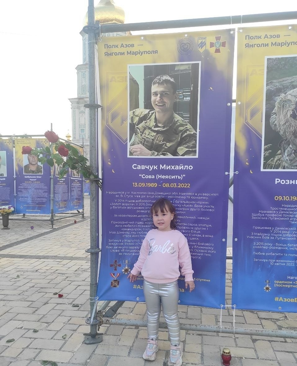 Ярослава показує фото свого татка на банері. Дівчинка знає, що він - герой і нині став янголом, але дуже сумує за ним