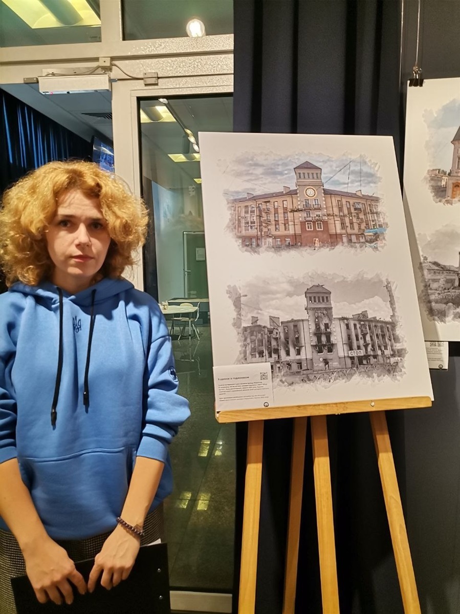Алевтина на виставці біля малюнка свого будинку